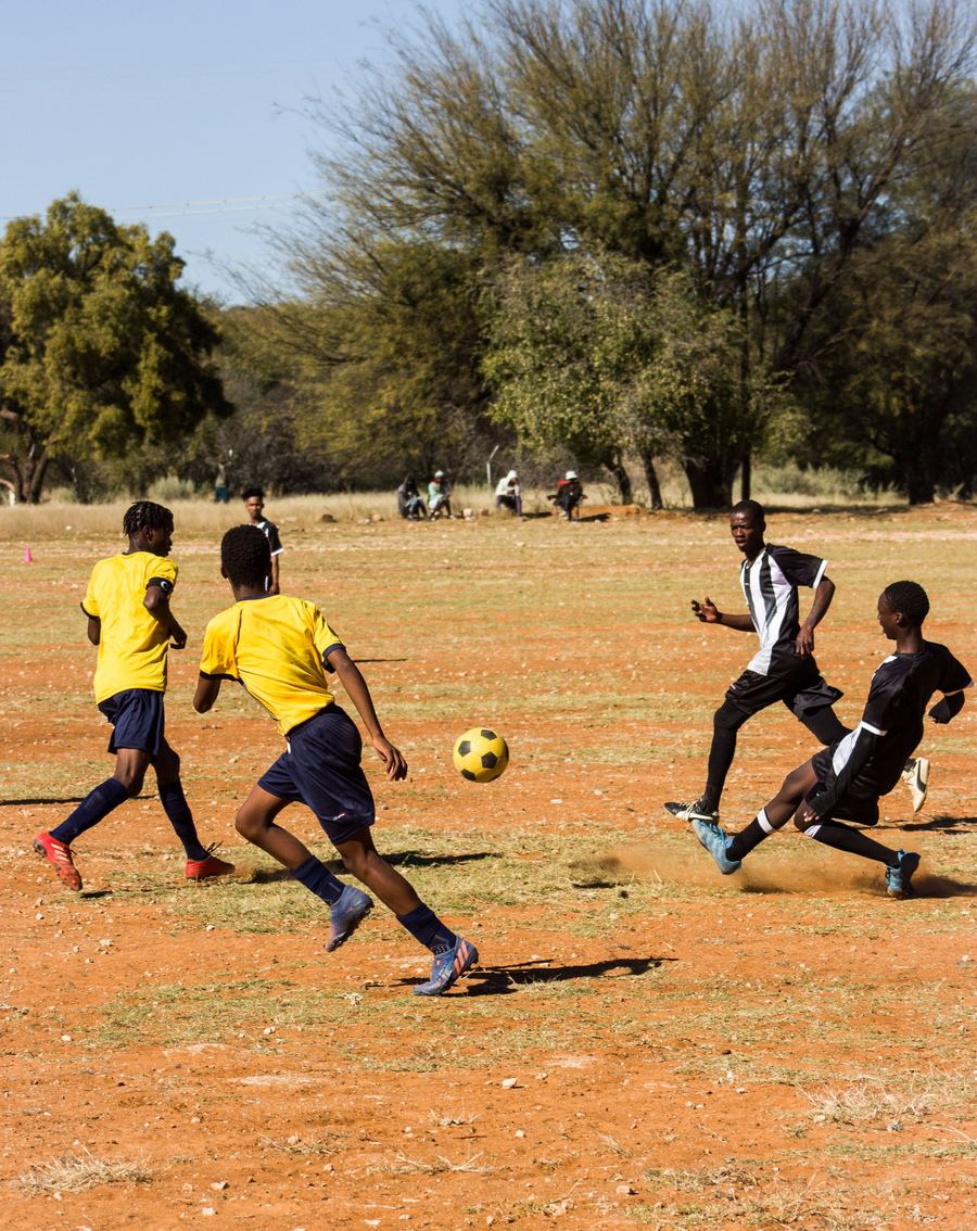 Jeunes joueurs en maillots jaunes et noirs jouant au football sur un terrain en terre